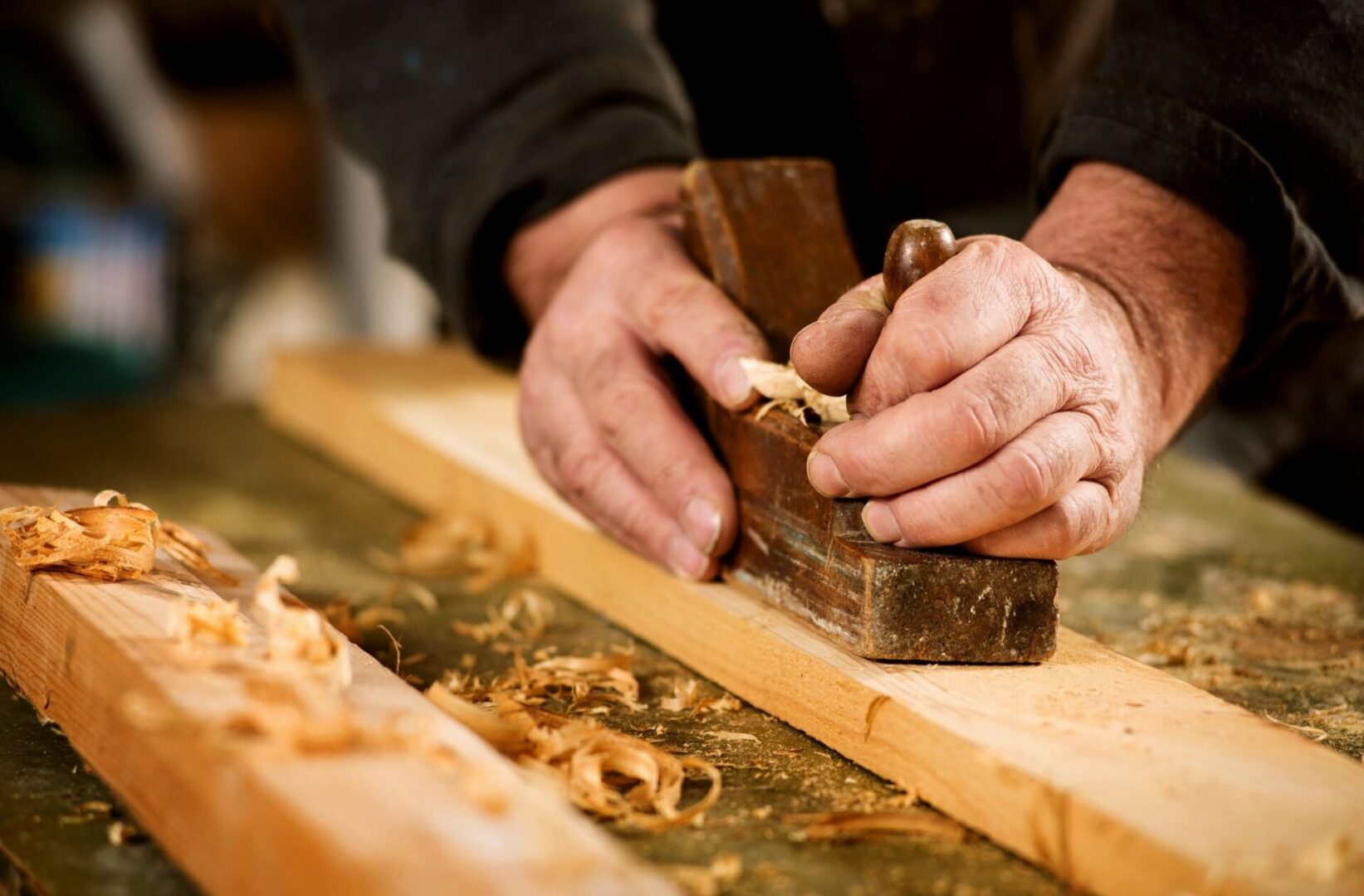 A person using a wood plane on a wooden board.